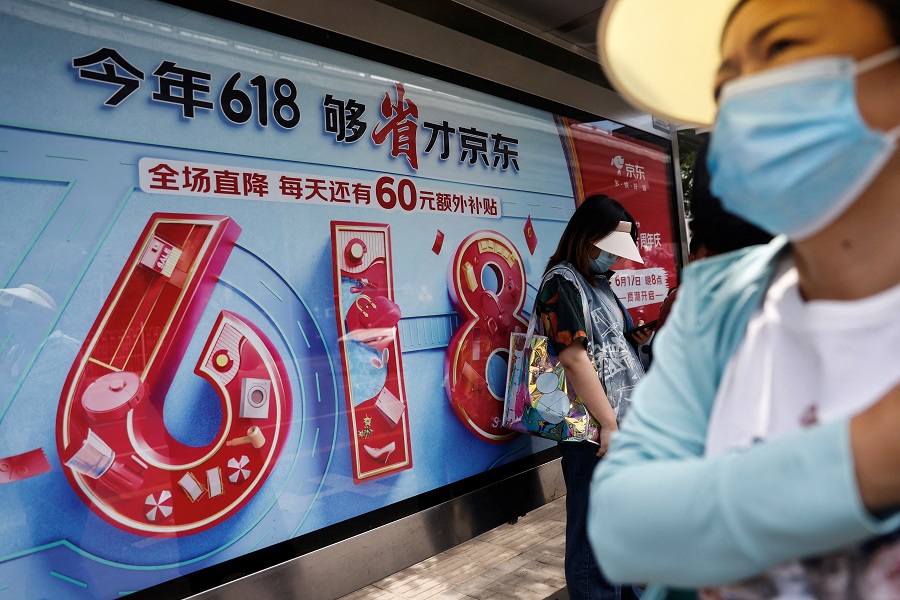 People near a billboard of JD.com's advertisement for the 618 shopping festival, in Beijing, China, 12 June 2023. (Tingshu Wang/Reuters)